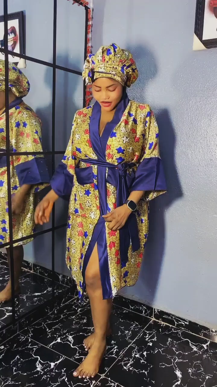 Load video: Radiate elegance and cultural flair with this stunning robe set, crafted from silk Ankara fabric with a luxe satin finish. Featuring a bold floral print in vibrant hues of gold, red, and blue, this robe brings together tradition and modern femininity. The rich navy satin trim and belt add a touch of regal contrast, while the matching hair bonnet completes the look in flawless style. Whether for lounging, bridal prep, or gifting, this set is made to make you feel powerful, polished, and beautiful.